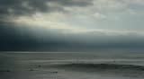 Wave breaking in slow motion under stormy skies with birds and surfers.