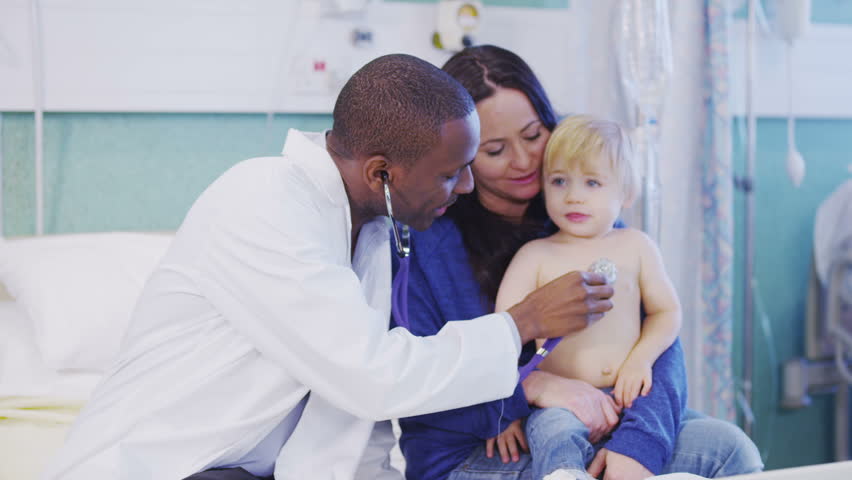 Very cute little boy sits on his mother's lap while a doctor listens to his heartbeat. In slow motion.