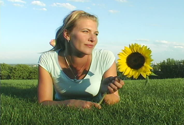 Video of a blond girl with a sunflower in a natural surrounding with plenty of space to ad your own elements and wordings