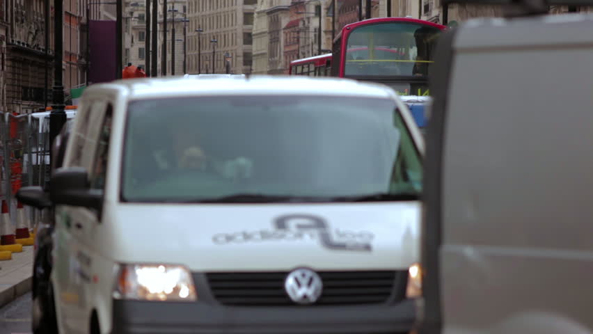 Stationary shot of London busy daytime traffic on a street. Buses, cars, taxis wait in line for the green light. Then the pedestrians cross the street. 