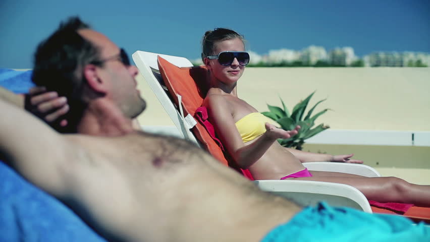 Young couple lying on sunbed and applying sun cream
