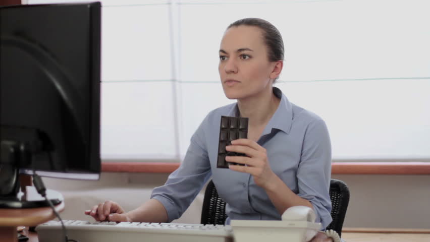 Young business woman eating chocolate at workplace