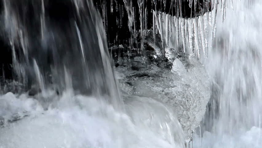 Icicles and running water at small waterfall. Focus on icicles.