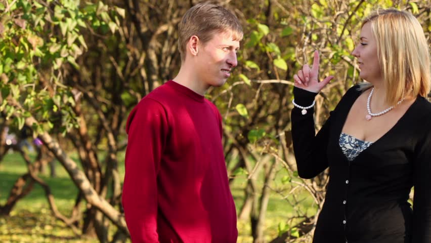 Young blonde woman imitates  shooting a gun with finger of man in park at sunny autumn day