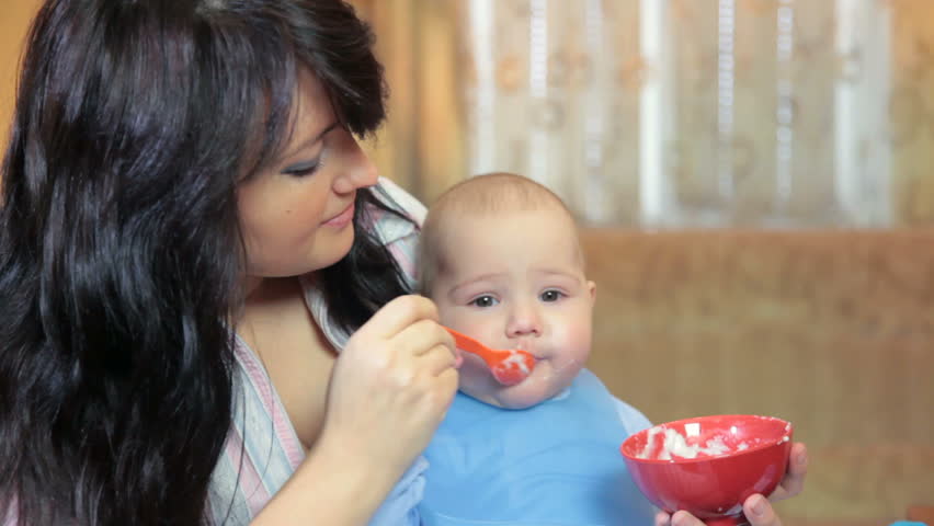 Young mother feeding her baby boy at home