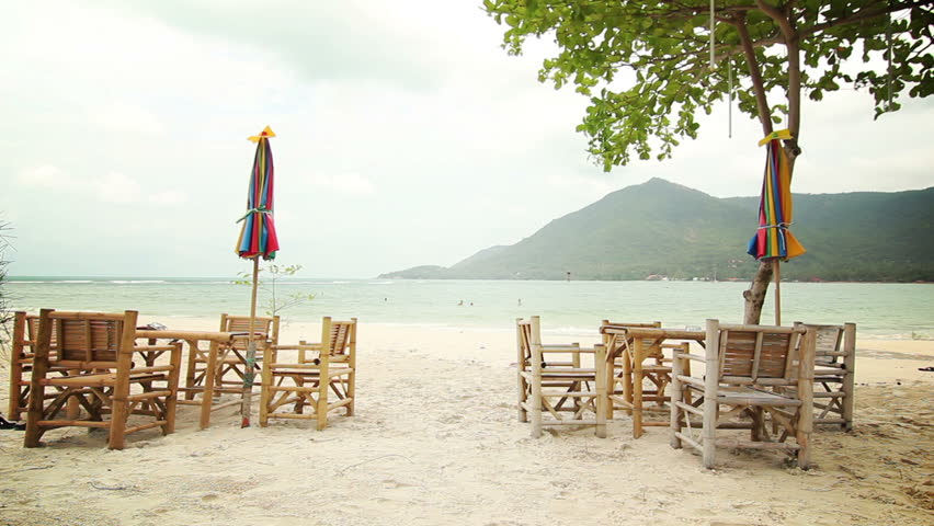 Empty Beach Cafe - Wide angle shot of beach bar seating (bamboo chairs and tables) with island bay in the background