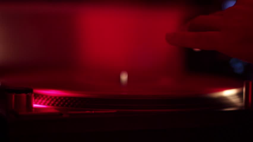 DJ hand places stylus on a turntable vinyl record scratches platter in nightclub