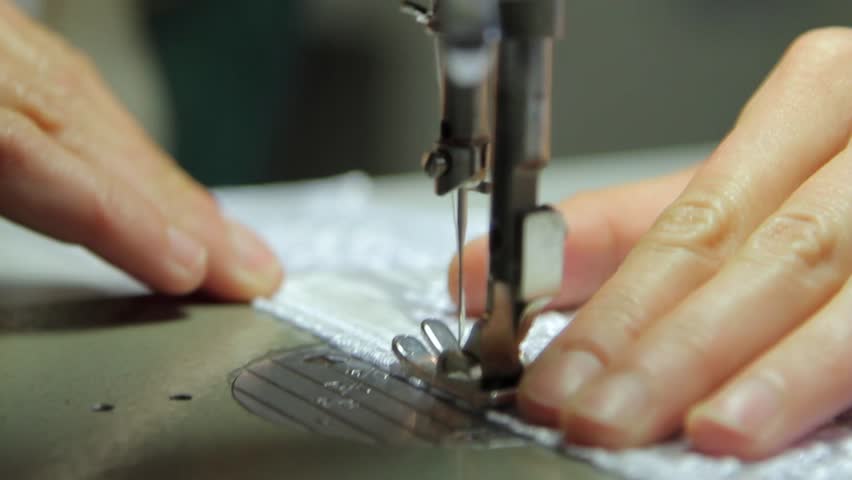 A hand of a dressmaker supporting a cloth while sewing on a sewing machine.