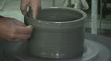 Two hands are molding clay into a vase.