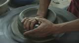 Two hands are molding clay into a vase.