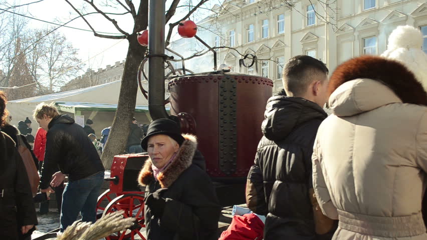 VILNIUS, LITHUANIA - MARCH 02: Huge retro steel pot on wheels and hot wine boil smoke vapour rise and lot of people walk in outdoor street spring event festival on March 02, 2012 in Vilnius.
