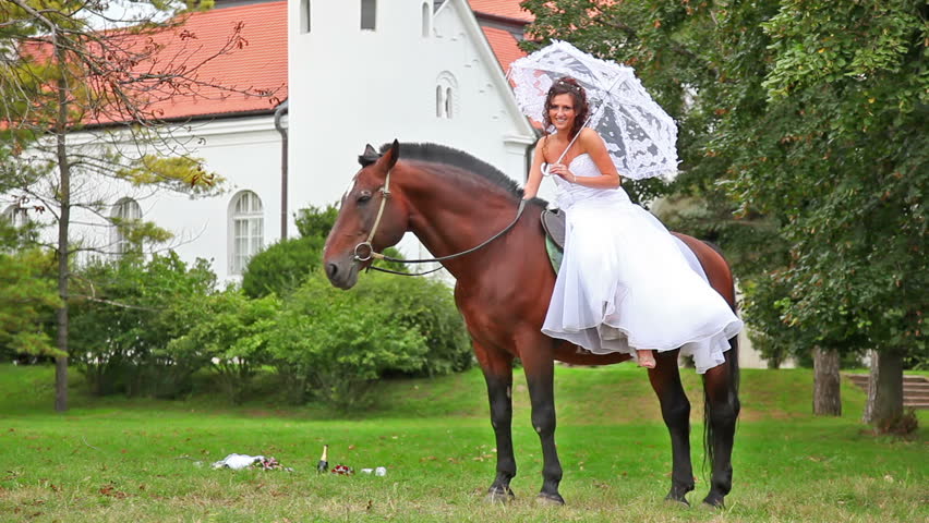 Happy bride riding a beautiful brown horse in the garden