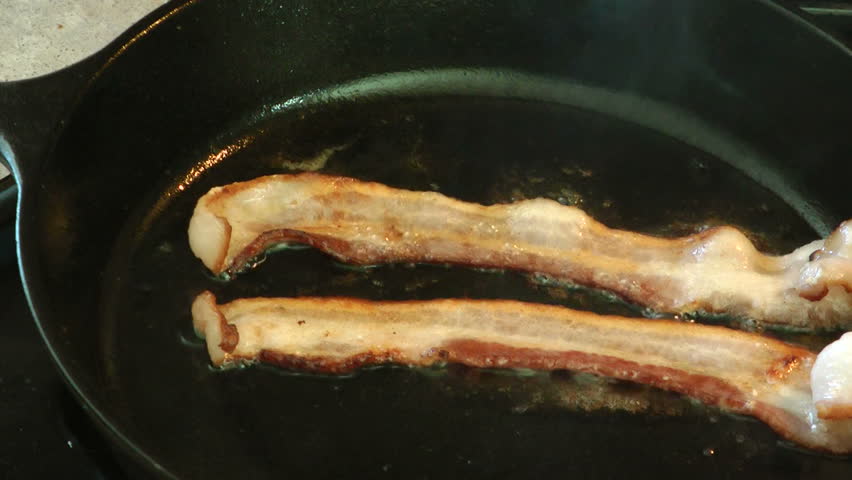 Delicious bacon frying in a cast iron pan