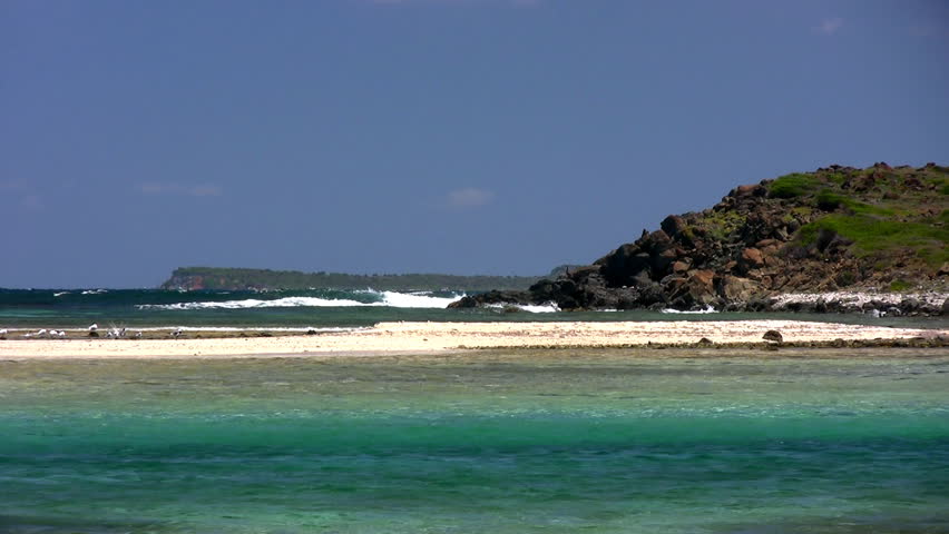 A view from a Caribbean Island with a beautiful horizon with seagulls resting on a sandbar and waves crashing against rocks