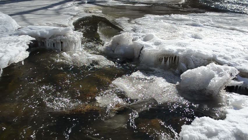 wondeful wild creek cataract rapid water flow between frozen ice and icicles beautiful sunlight.