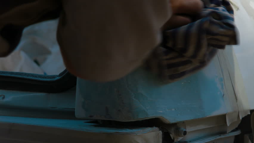 Repairman is preparing car surface for smearing putty, wiping it with a cloth.