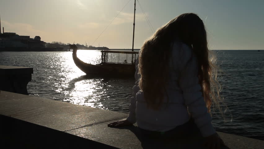 Little girl sitting on the embankment at sunset Sevastopol