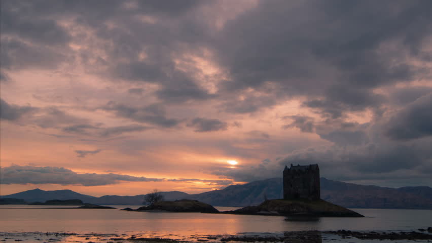 Sunset and moving clouds behind Castle Stalker in Scottish highlands. Time lapse, zoom in and pan right.