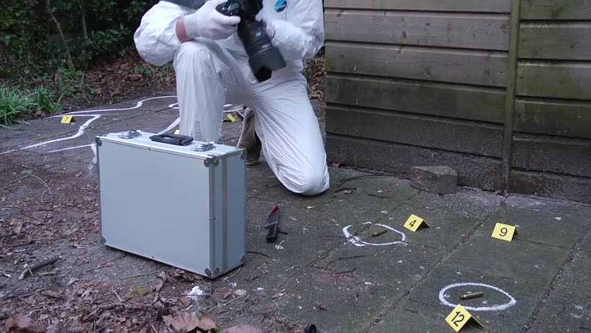 Forensics police investigator taking photos of the evidence, marked by chalk circles and evidence markers, weraring a white suit, carrying an aluminum suitcase