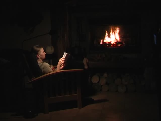 Woman sitting in front of a fire, reading and enjoying a glass of wine