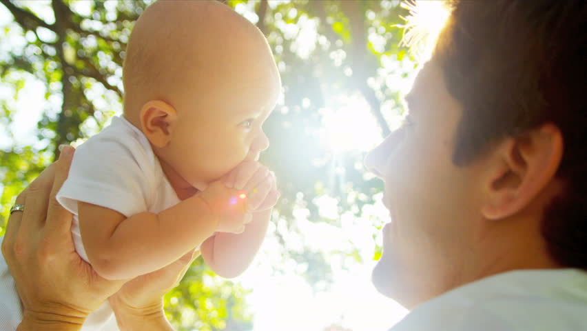 Young Caucasian father lovingly holding up cute baby while they play together outdoors