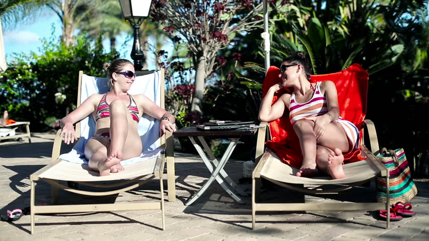 Young women lying on sunbed and talking
