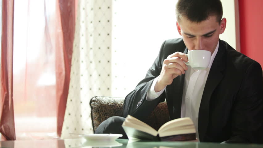 Young guy reading a book and drinking coffee
