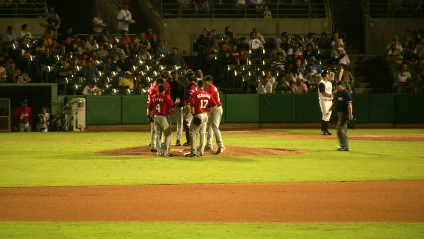 Video of baseball stadium from the outfield. Team on pitcher mound and running back to positions. Night time with glowing playing lights. Stadium full of spectators. Don Despain of Rekindle Photo