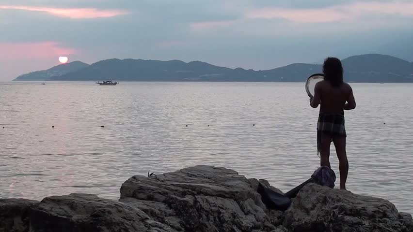 KAS, TURKEY â 12 August 2012: Aboriginal music concert at the Buyuk Cakil Beach - A man is singing a meditating song and playing on the declining sun, a boat is passing, audio