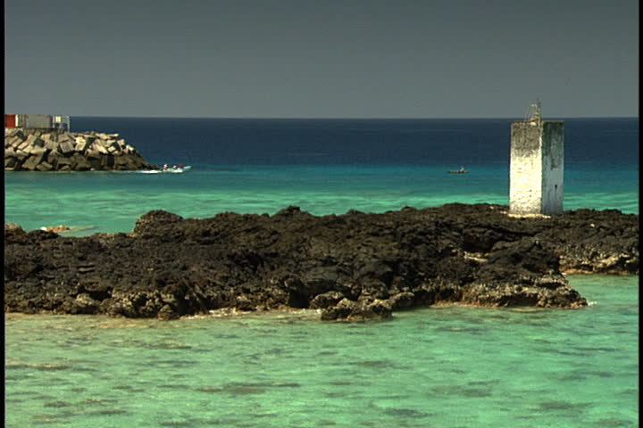 MORONI, UNION OF THE COMOROS (COMOROS ISLANDS), AFRICA - CIRCA NOVEMBER 1998: Turquoise blue water and rocky sandbar with remains of a lighthouse. A speedboat passes in the distance.