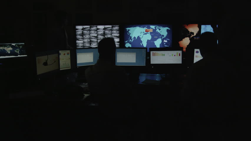 A team of male security personnel working within a busy system control room. This could be a weather station/airport traffic control room. It could be a  power station or police/army control facility.