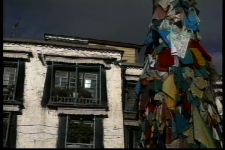 LHASA, TIBET - OCTOBER 01, 1993: Pole covered with prayer flags, pan over to villagers and monks walking past smoldering bonfire.