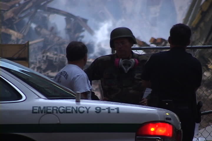 NEW YORK CITY - SEPTEMBER 28, 2001: Three emergency workers speaking together in front of rubble. They split apart and police officer walks to cruiser in foreground.
