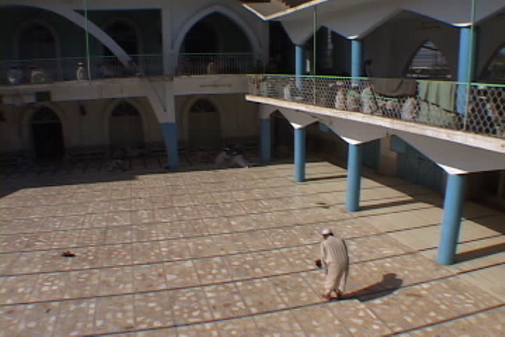 PESHAWAR, PAKISTAN - NOVEMBER 01, 2001: Lonely figure in Muslim dress bows and kneels down to pray in courtyard.