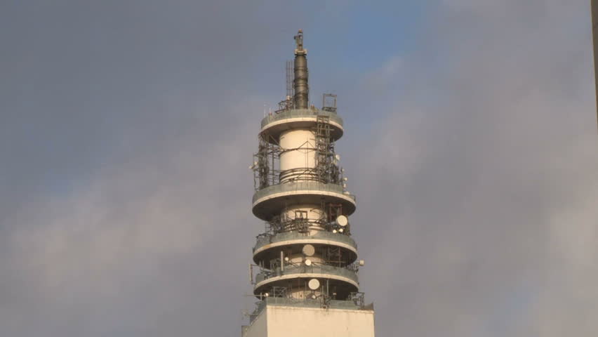 Dark clouds passing behind the top of a communications satellite tower in timelapse.