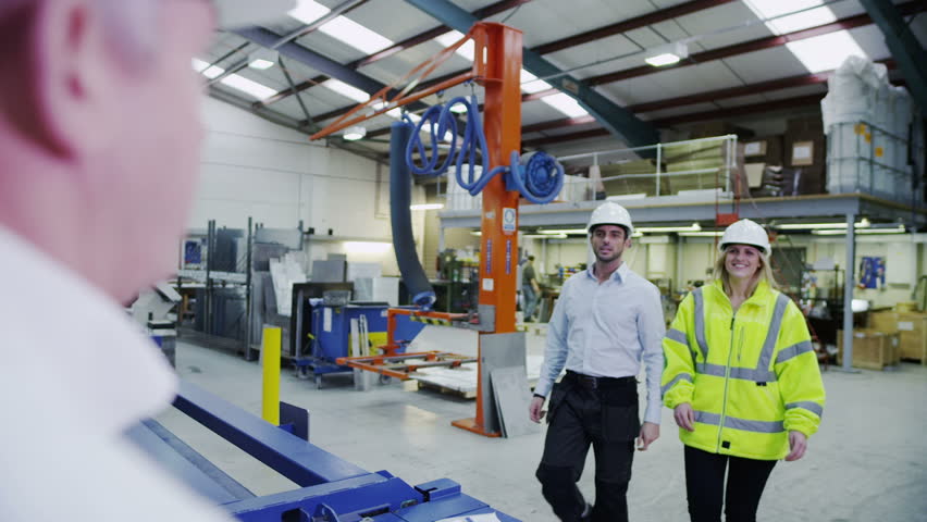 Male and female warehouse or factory workers, in high visibility clothing and hard hats take instructions from their manager. In slow motion.
