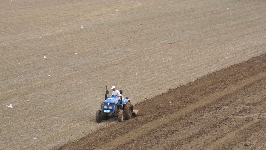 HEILONGJIANG PROVINCE, CHINA - CIRCA MAY 2013: Tractor plowing the field (01). Chinese farmer on a small tractor plowing a field in spring day. Static long shot. North China, Heilongjiang Province, May 2013.
