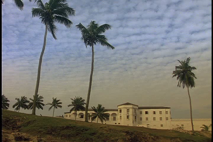  WS Elmina Castle in Ghana, Africa, with palm trees in foreground, under a mottled cloudy sky