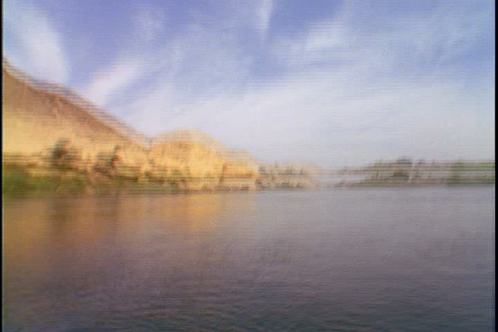 Scenic shots of the Nile River in Egypt; POV shot from fast moving boat. Camera tilts up from surface of water to desert hills under bright blue sky, then back down to surface again.