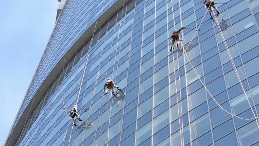 Four workers hang on ropes and wash windows of skyscraper, view from below