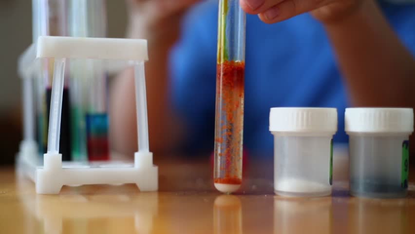 Young boy pours chemical reagents which is precipitates in test tube with liquid, focus at fingers and tube