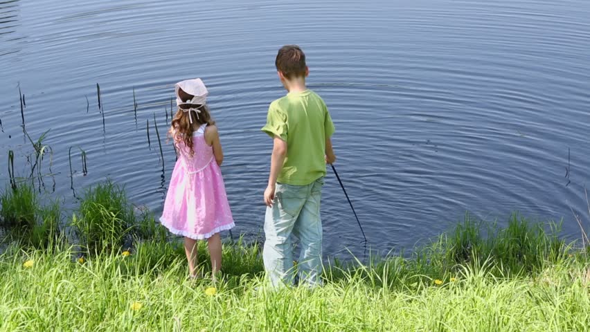 Two kids boy and little girl stand near pond and beats water surface by fishing rods