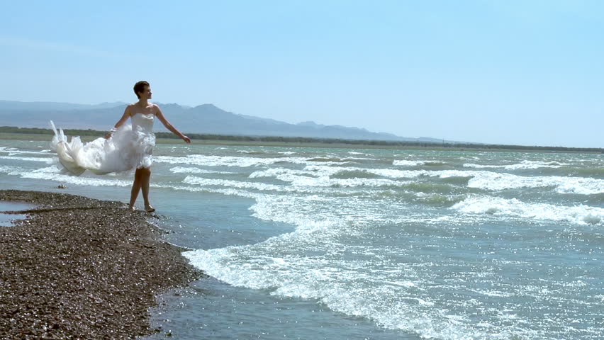 Honeymoon at Sea. Woman in a wedding dress walking along the edge of the surf. Slow Motion at a rate of 240 fps
