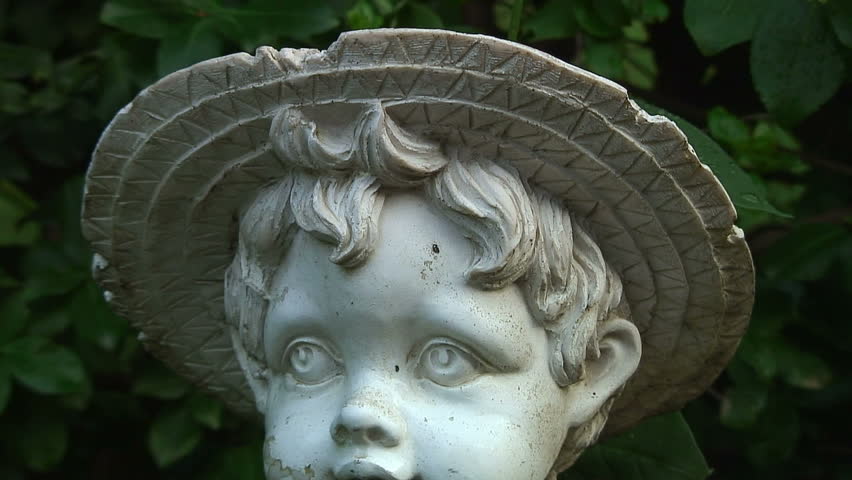 A decaying statue of a young child holding a bucket wearing a hat and overalls. HD 1080