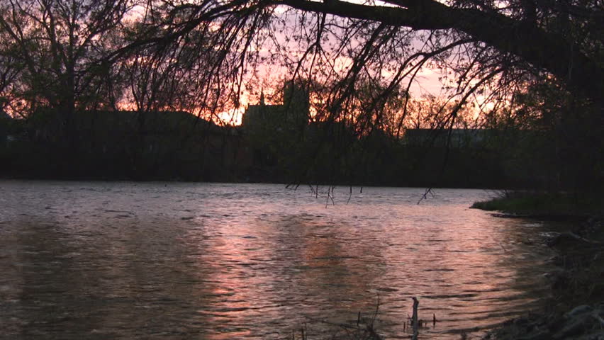 The reflection of a sunset on a flowing river, with the shadow of a church in the background.
