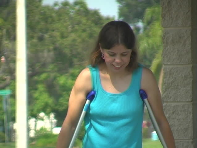 A woman walks toward the camera with crutches outdoors.