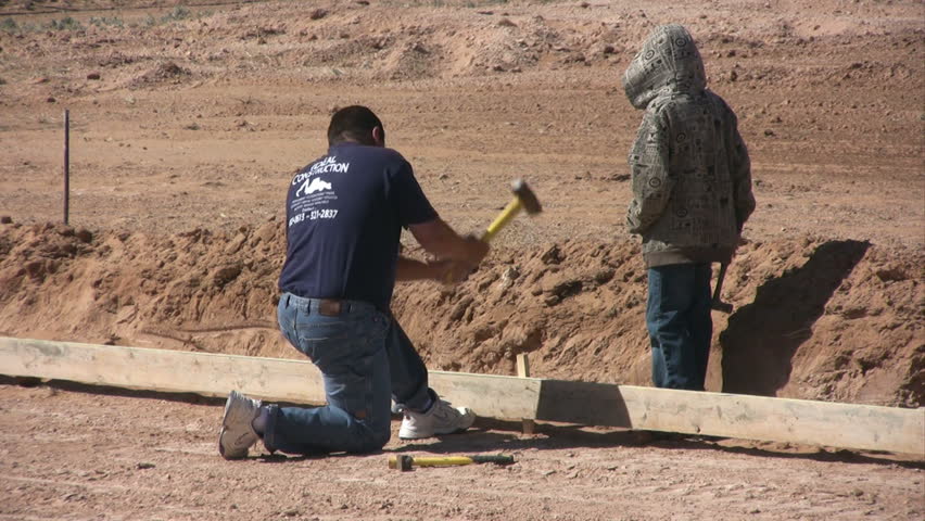 A man and his son work together to drive steel stakes for forms on a new home foundation.
