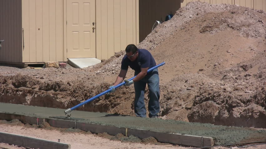 A man using a bull float to smooth cement. while another man sprays water from a hose.
