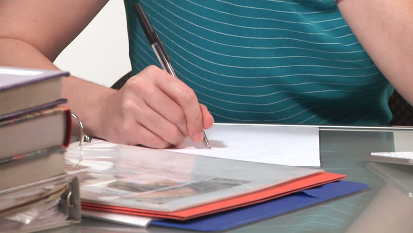 young woman writes and does homework at a desk piled with books