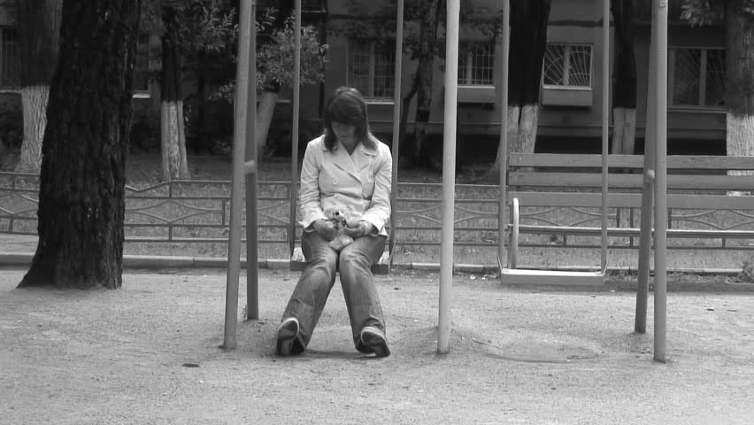Alone woman in deep depression on a swing with Teddy bear. Black and white.